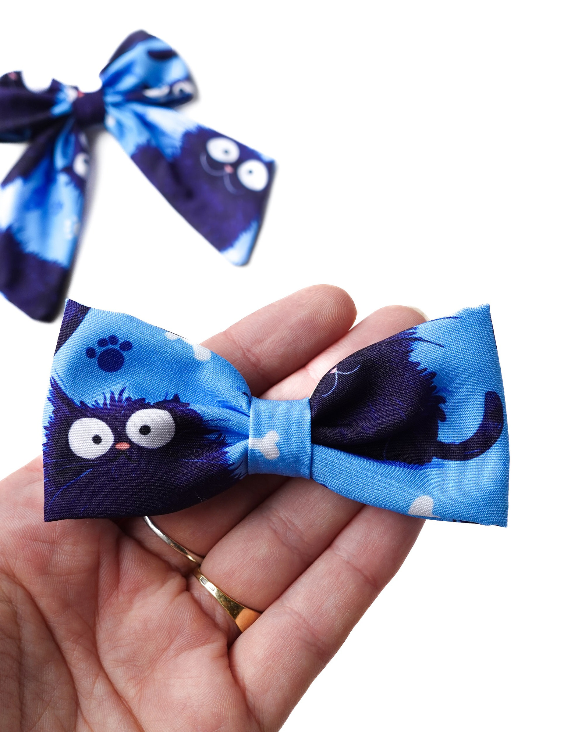 blue cat bow hand Close-up of handmade blue fabric hair bow with playful cat print, shown on hand for size reference.