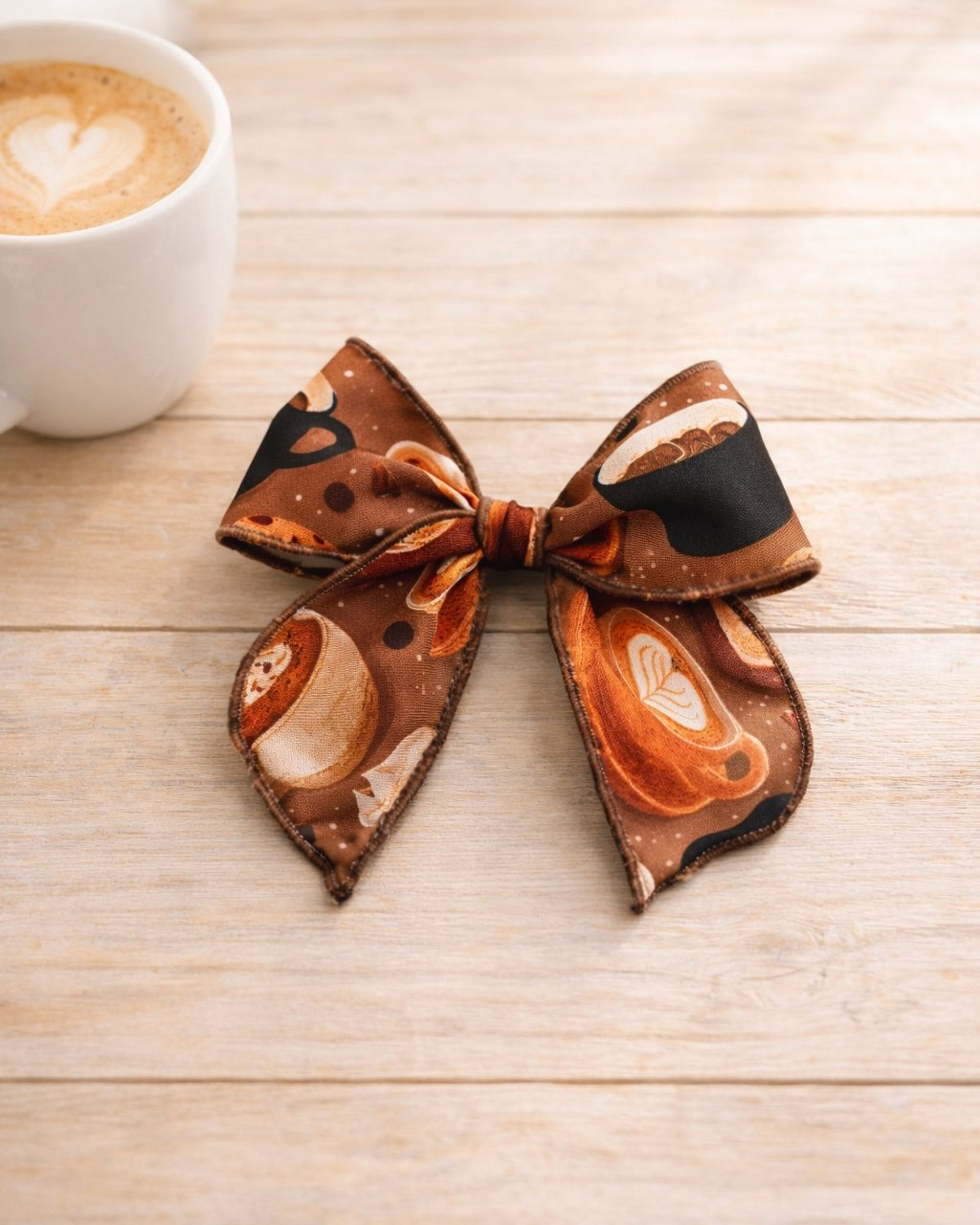 coffee bow Brown fabric bow with a coffee-themed print on a light wooden surface.