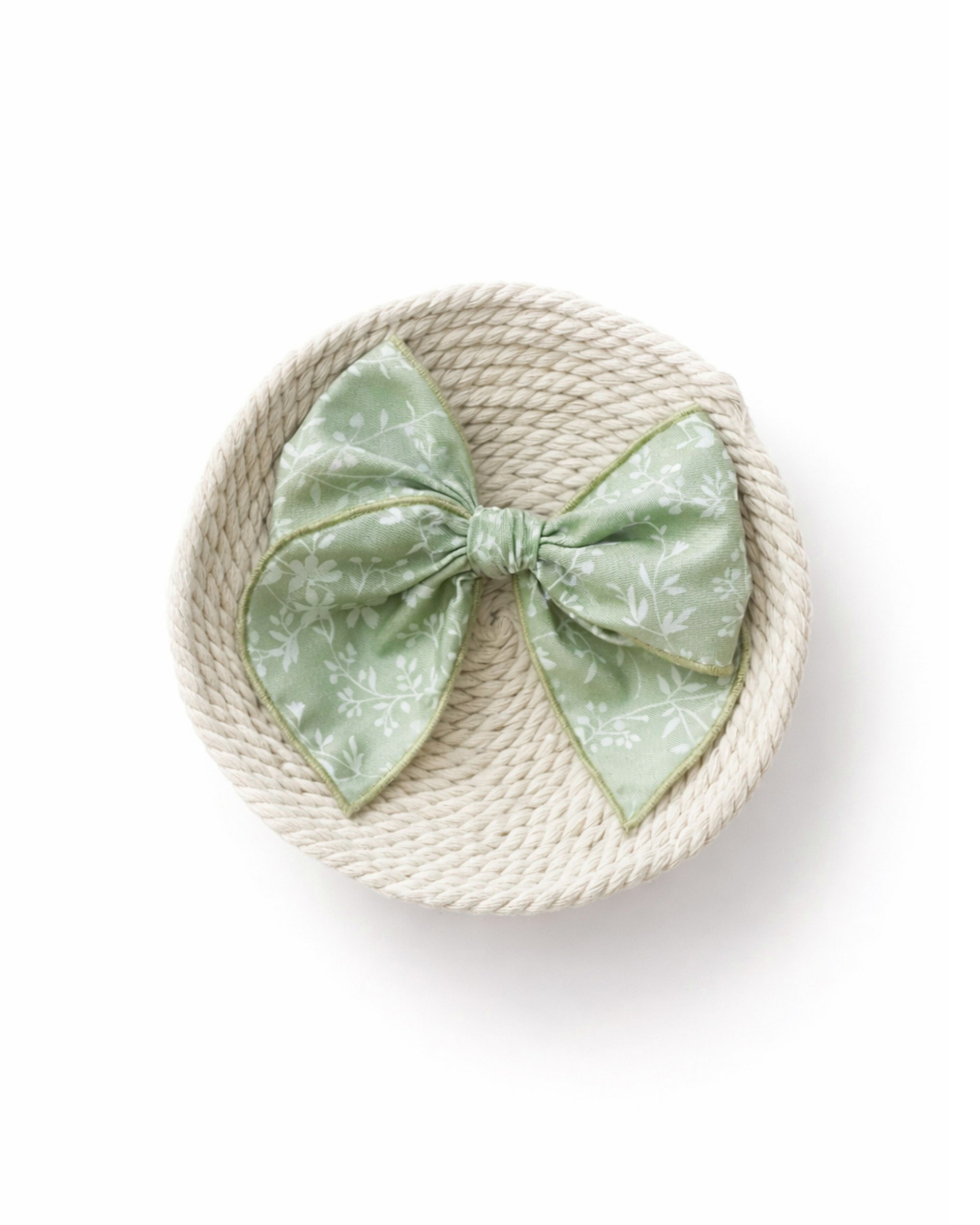 green bow white lives Close-up of sage green handmade hair bow with leafy print and rolled edges.