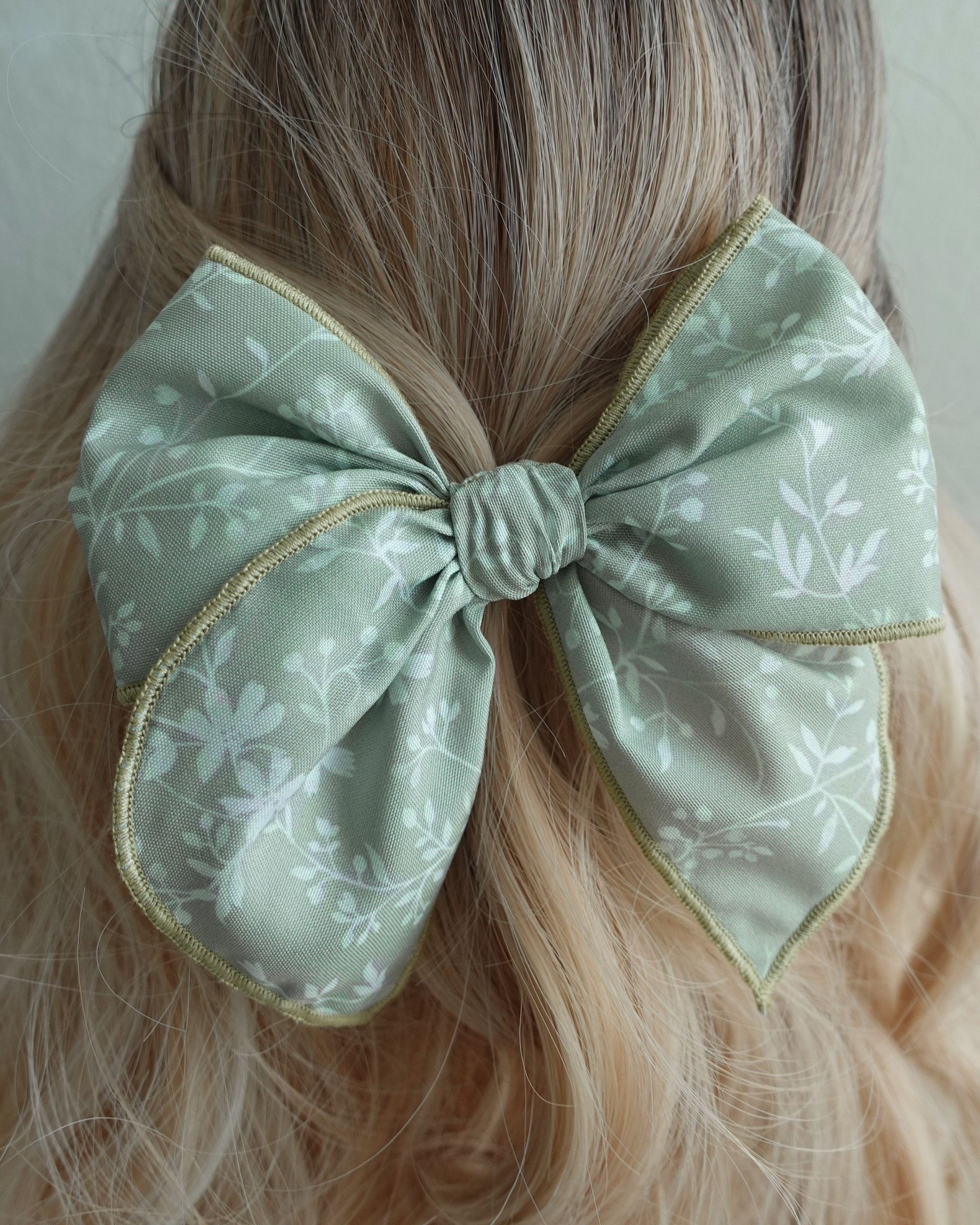 green bow eith leafs Close-up of sage green handmade hair bow with leafy print and rolled edges.