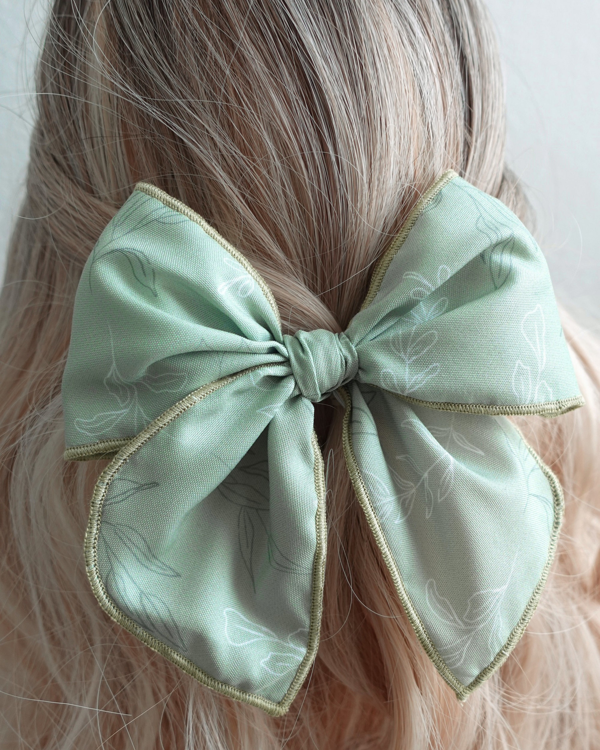 soft sage green bow Close-up of sage green handmade hair bow with leafy print and rolled edges.