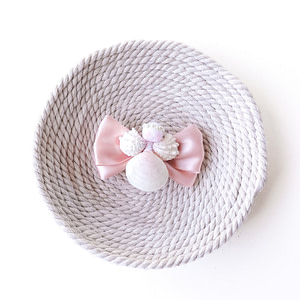 Handmade pink satin hair bow with seashell angel decoration on neutral woven background
