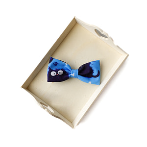 Handmade blue fabric hair bow with cute cat print, displayed on a wooden tray.