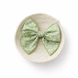 Home Sage green handmade hair bow with leafy print and soft rolled edges.